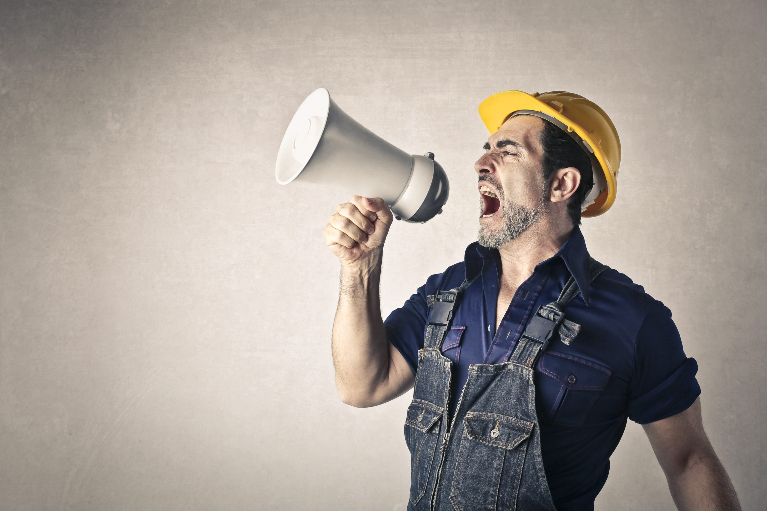 Un homme en tenue de chantier criant dans un mégaphone