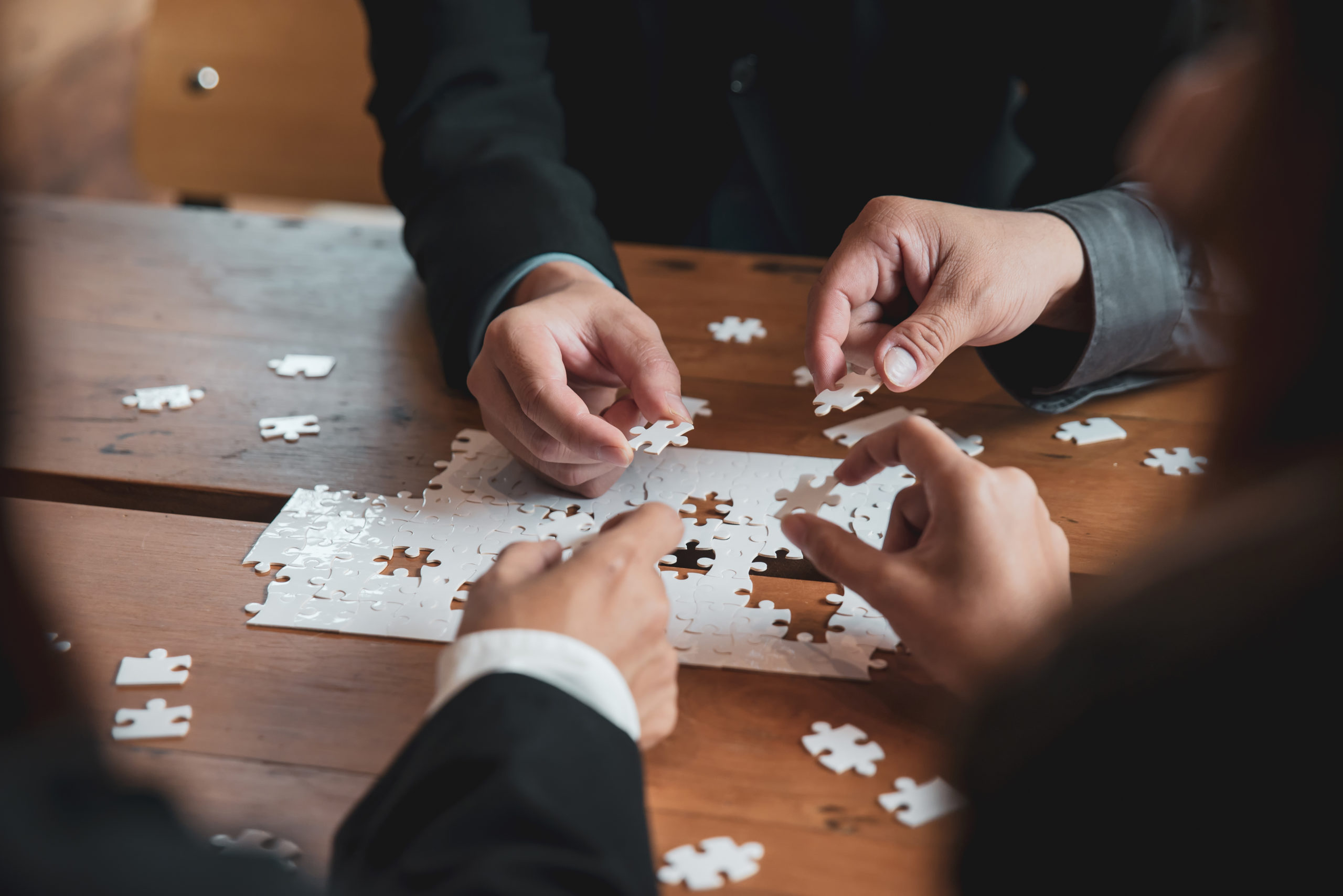 Plusieurs mains assemblent des pièces de puzzle sur une table en bois