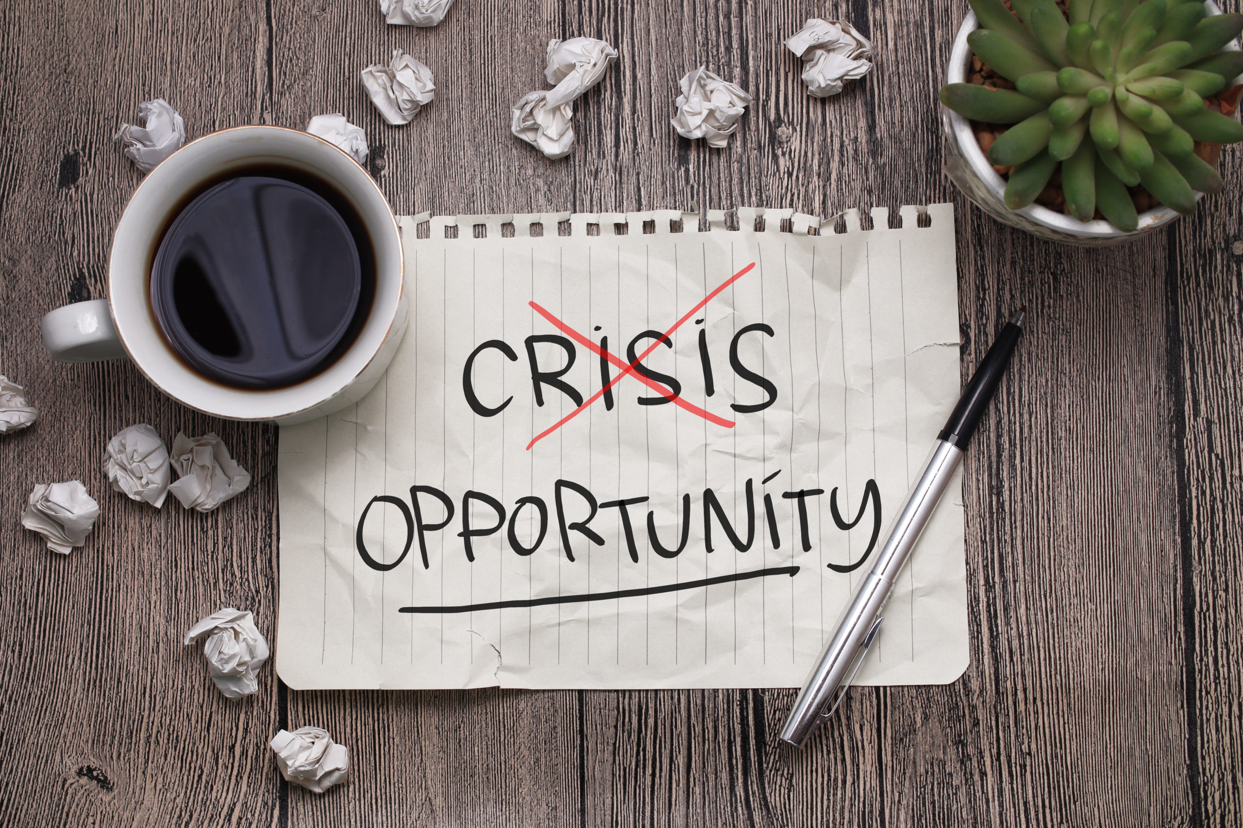 Une feuille sur laquelle il est indiqué "Crisis Opportunity" avec des bouts de papier froissés et une tasse de café