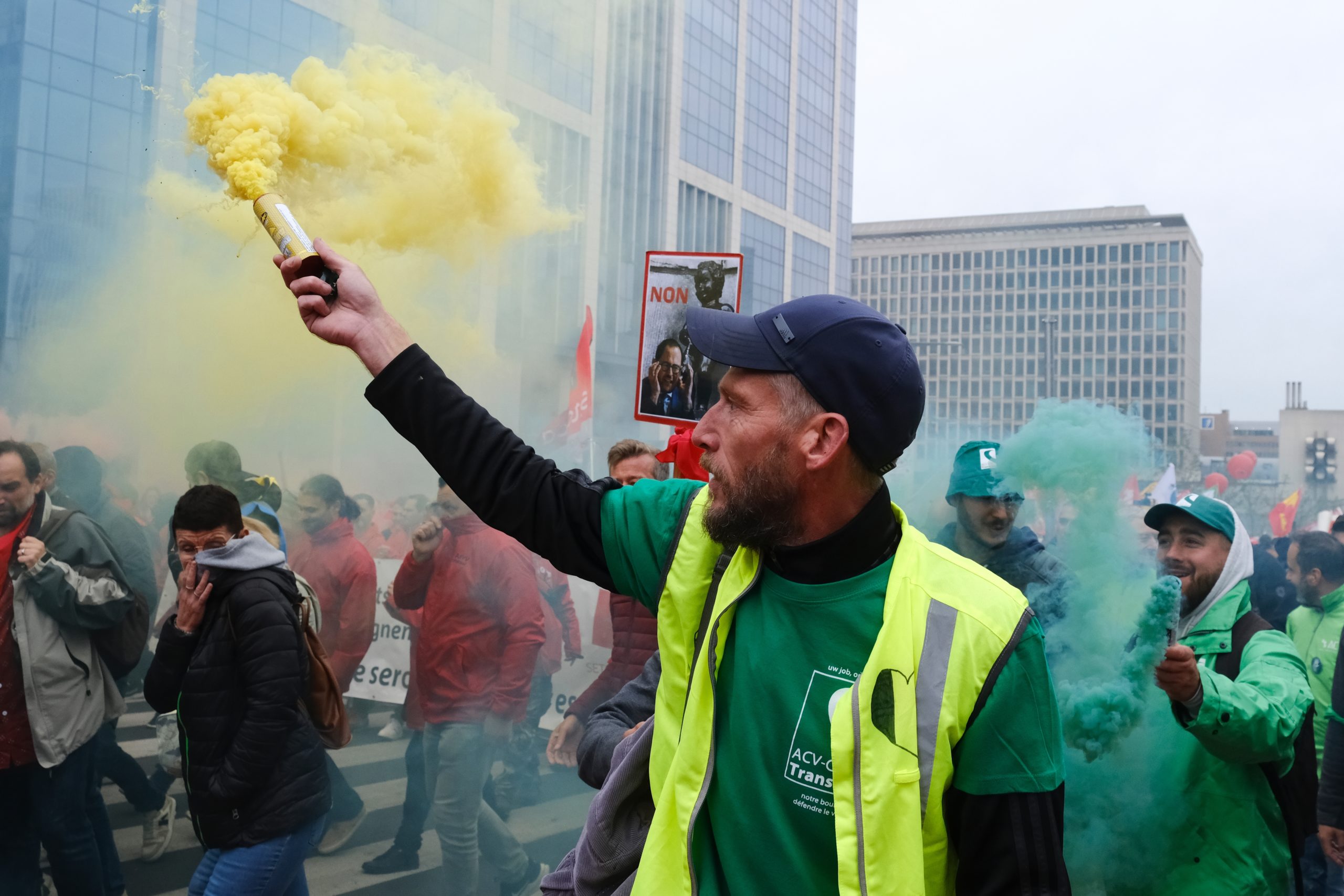 Manifestation de rue avec un homme brandissant un fumigène jaune, vêtu d'un gilet de sécurité