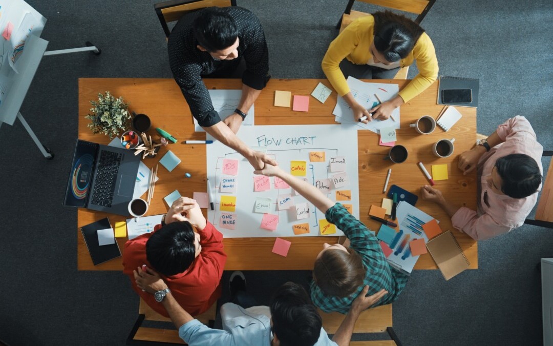 L'image montre un groupe de personnes autour d'une table en pleine négociation Deux personnes se serrent la main, symbolisant probablement un accord ou une coopération réussie.